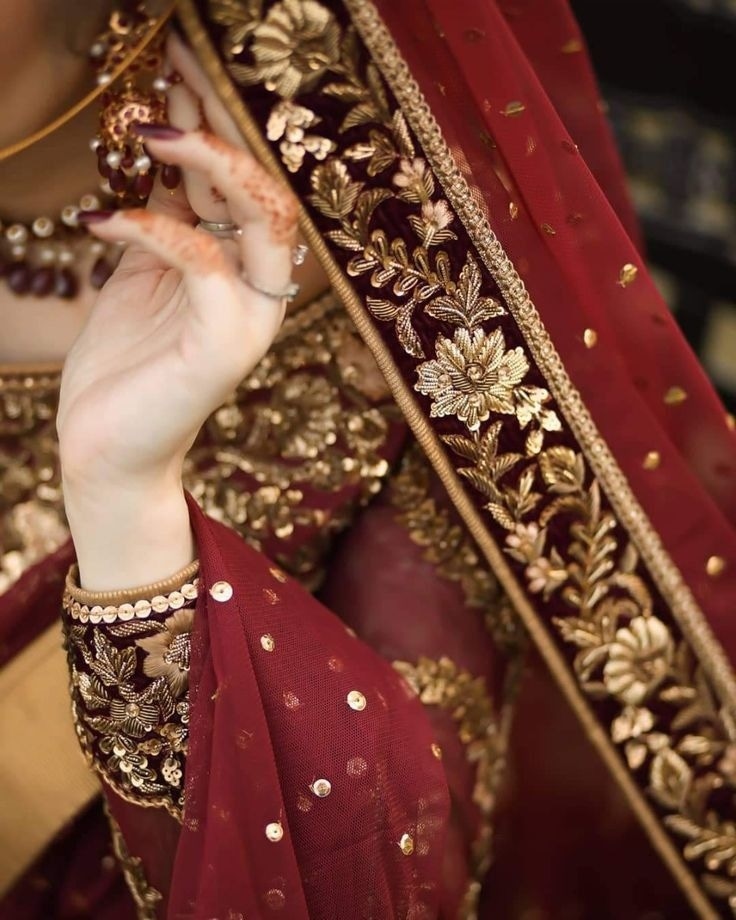Close-up of Indian bride's hand with intricate mehendi details and maroon dress